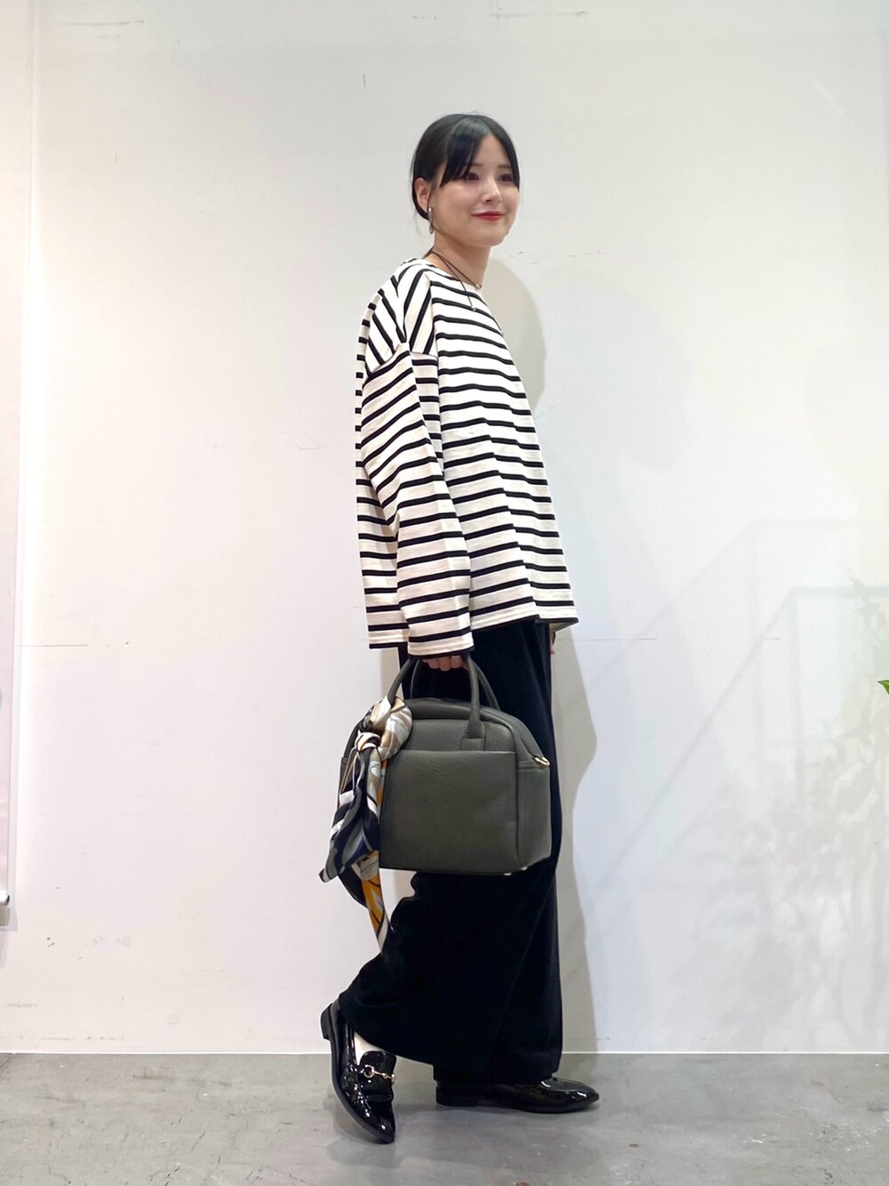 ホワイト系のTシャツ/カットソー、ブラック系のその他パンツ、グリーン系のボストンバッグを着用したレディースの秋コーディネートの2枚目の写真