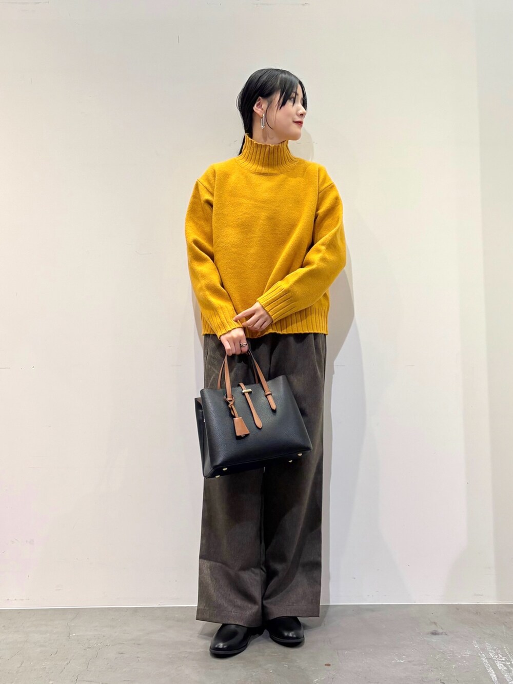 イエロー系のニット/セーター、ブラウン系のその他パンツ、ブラック系のトートバッグを着用したレディースの冬コーディネートの3枚目の写真