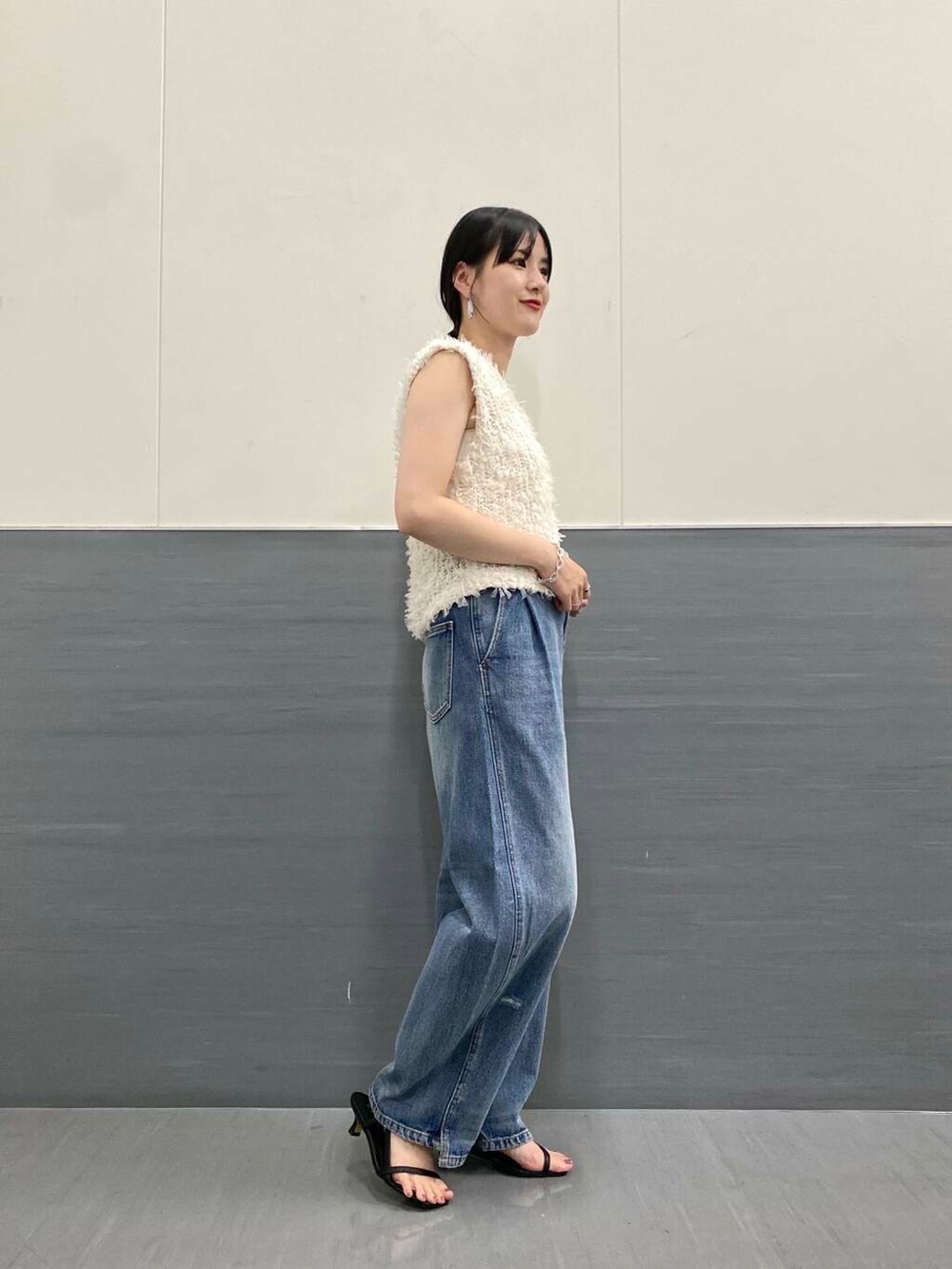 ブルー系のデニムパンツ、ホワイト系のベスト、ブラック系のサンダルを着用したレディースの夏コーディネートの3枚目の写真