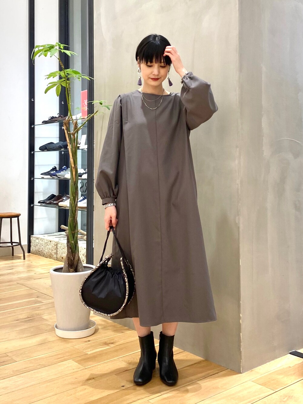 グレー系のワンピース、ブラック系のショルダーバッグ、ブラック系のブーツを着用したレディースの冬コーディネートの2枚目の写真