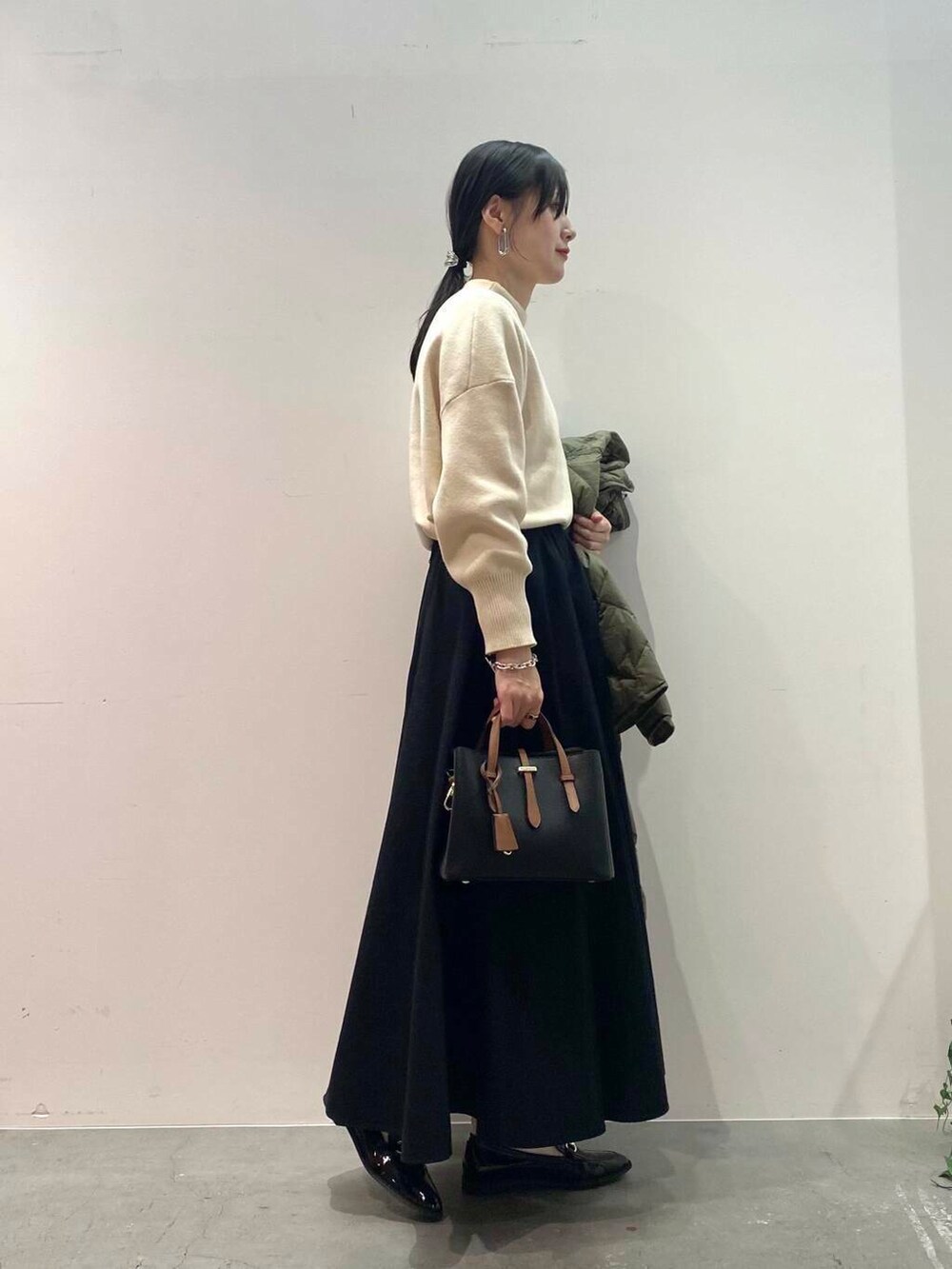 ブラック系のハンドバッグ、グリーン系のダウンジャケット/コート、ブラック系のローファーを着用したレディースの秋コーディネートの5枚目の写真