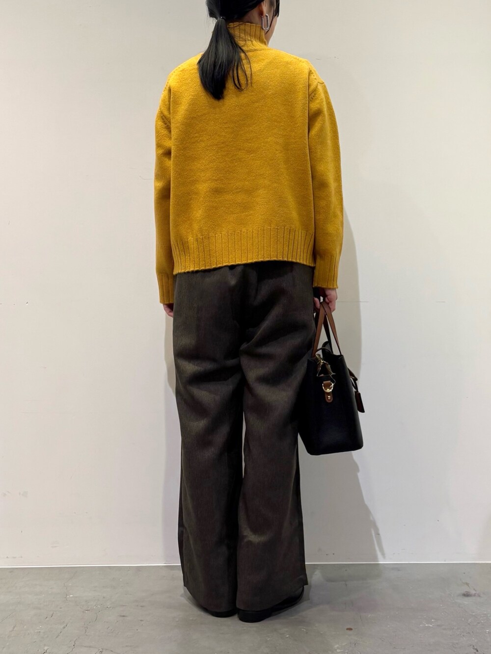 イエロー系のニット/セーター、ブラウン系のその他パンツ、ブラック系のトートバッグを着用したレディースの冬コーディネートの6枚目の写真