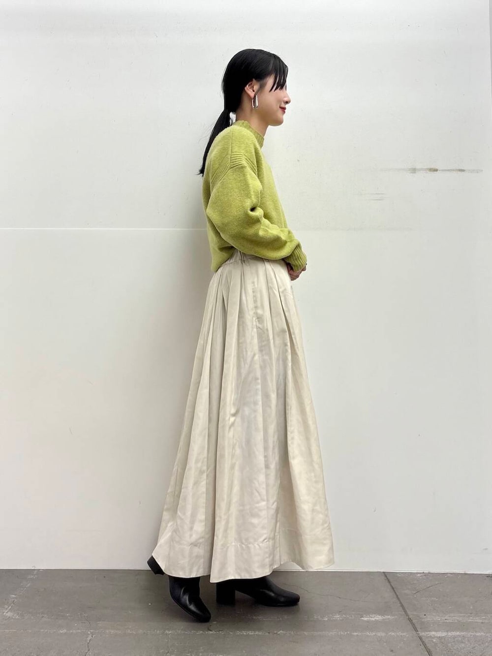 ブラック系のブーツ、ホワイト系のスカート、グリーン系のニット/セーターを着用したレディースの冬コーディネートの2枚目の写真