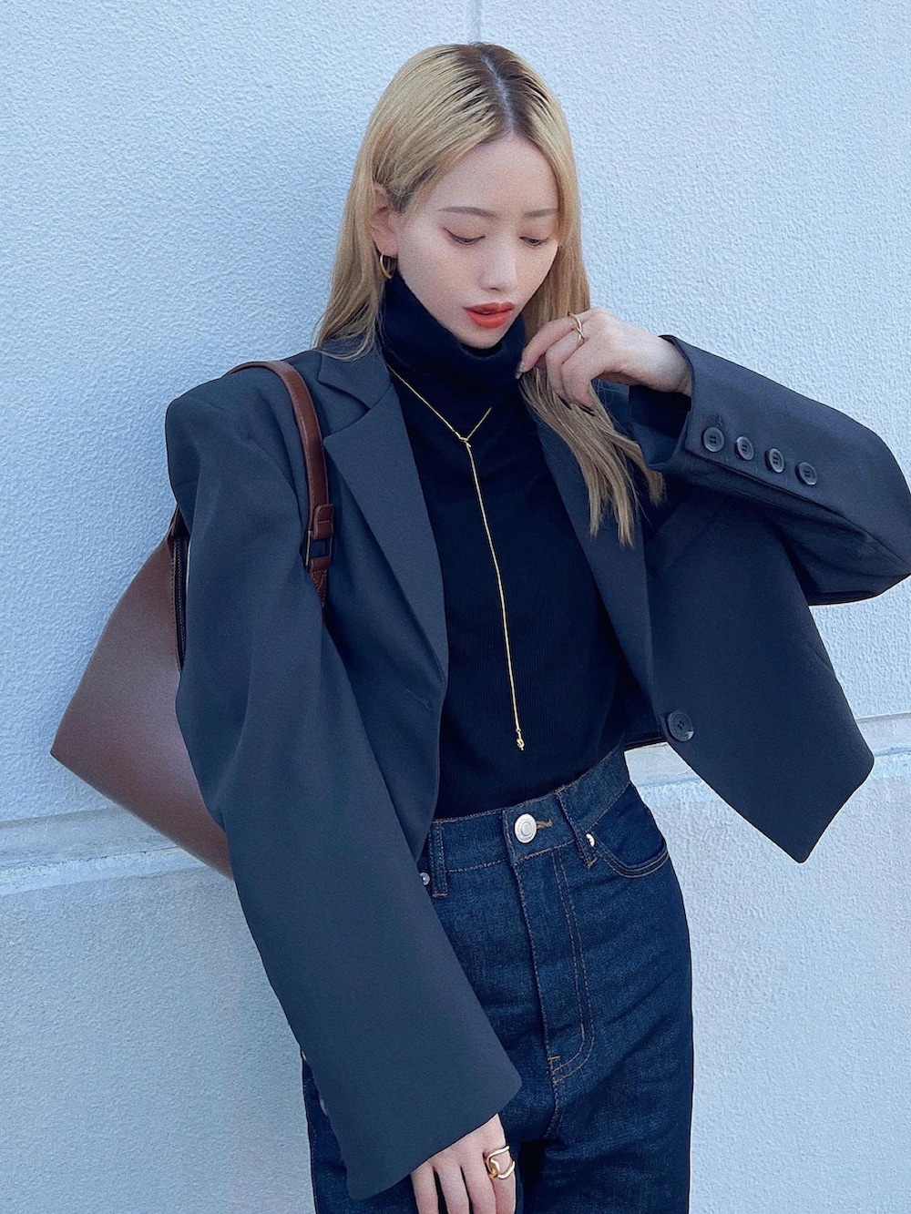 ブラウン系のハンドバッグ、ブルー系のデニムパンツ、ブラック系のスニーカーを着用したレディースの秋コーディネートの3枚目の写真