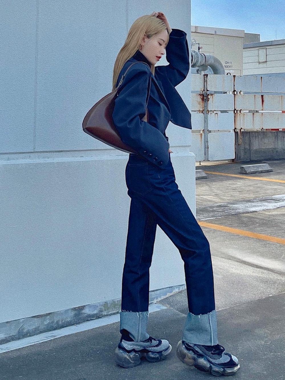 ブラウン系のハンドバッグ、ブルー系のデニムパンツ、ブラック系のスニーカーを着用したレディースの秋コーディネートの2枚目の写真