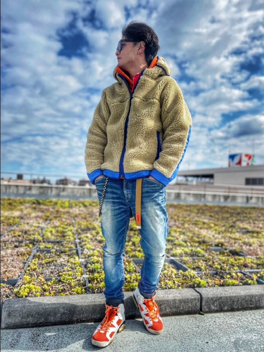 ベージュ系のブルゾン、ブルー系のデニムパンツ、オレンジ系のパーカーを着用したメンズの春コーディネートの2枚目の写真