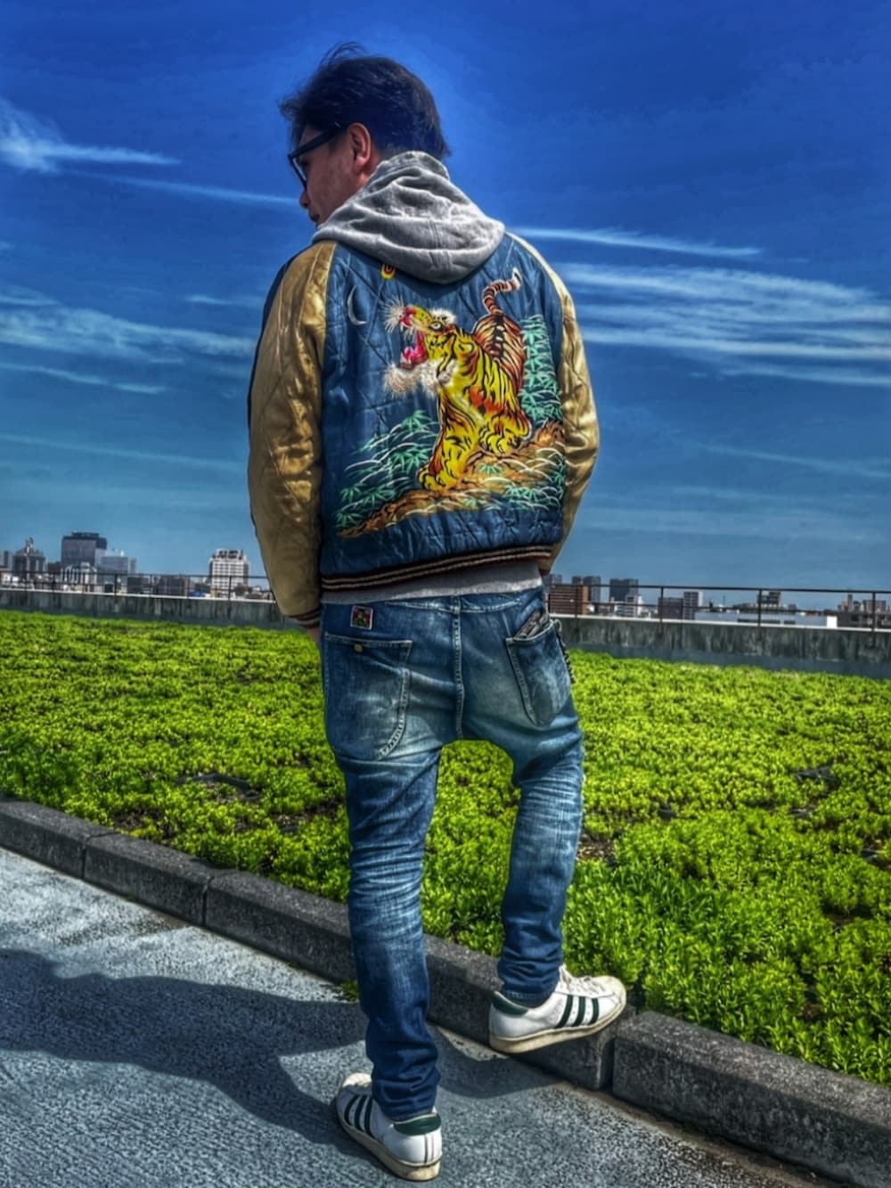 ブルー系のスカジャン、ブルー系のデニムパンツ、ホワイト系のスニーカーを着用したメンズの春コーディネートの2枚目の写真