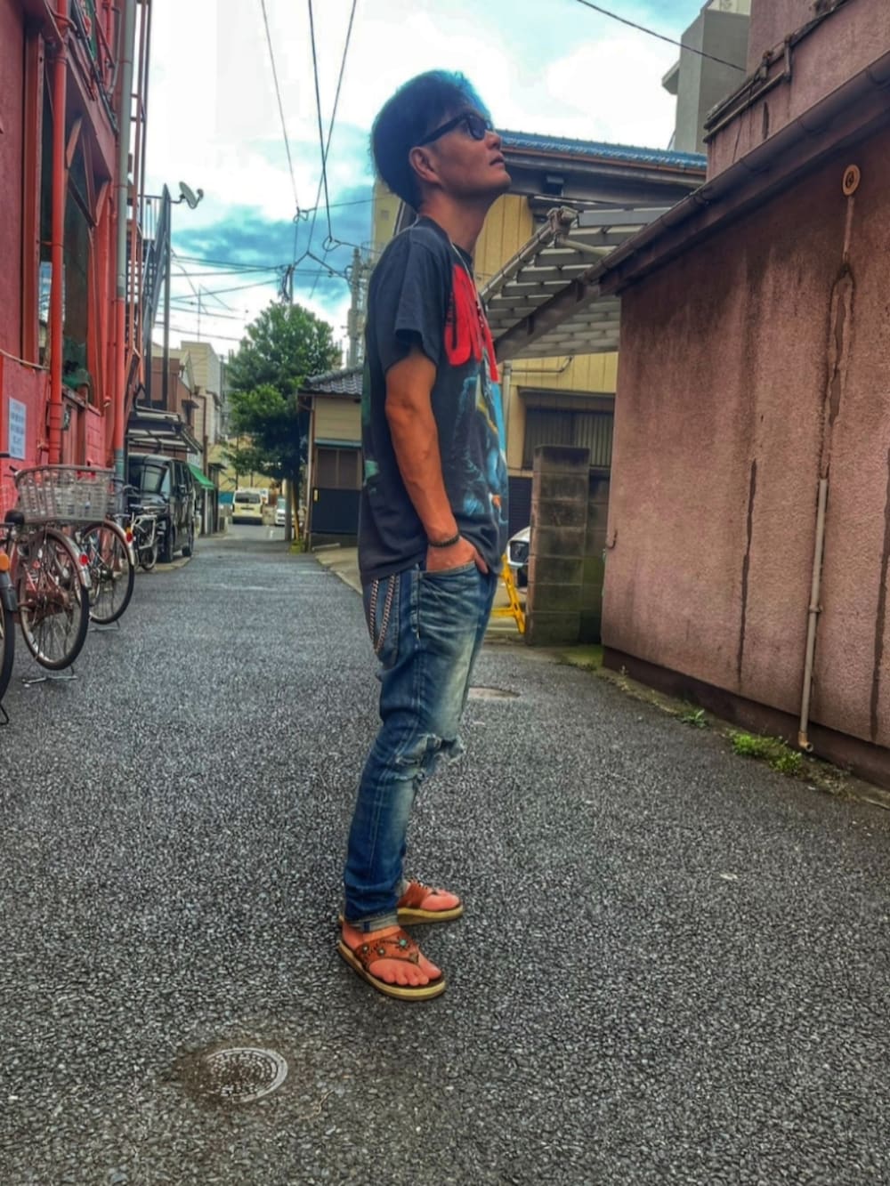 ブラック系のTシャツ/カットソー、ブルー系のデニムパンツ、ブラウン系のサンダルを着用したメンズの夏コーディネートの3枚目の写真