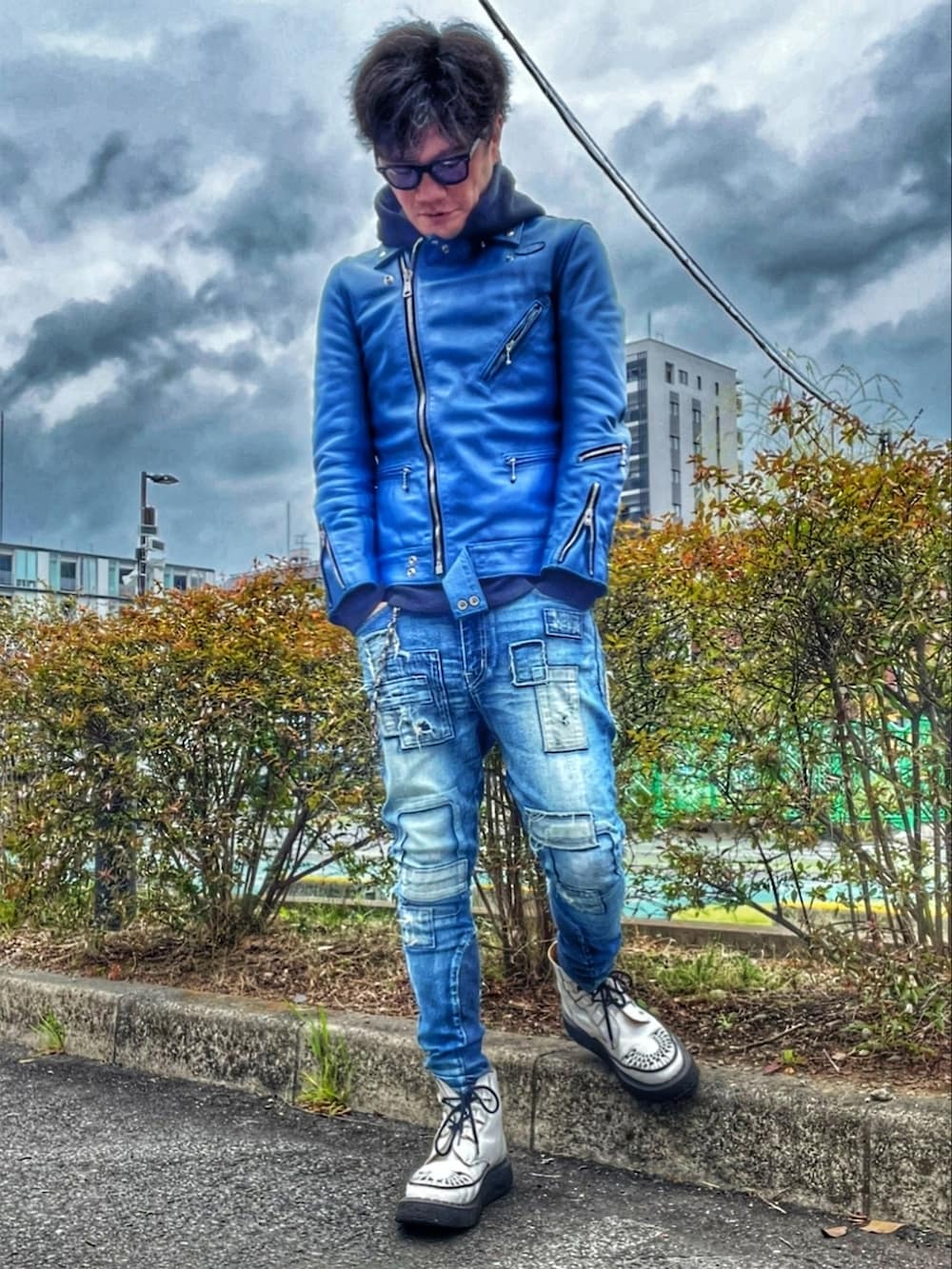 ブルー系のライダースジャケット、ブラック系のパーカー、ブルー系のデニムパンツを着用したメンズの春コーディネートの2枚目の写真