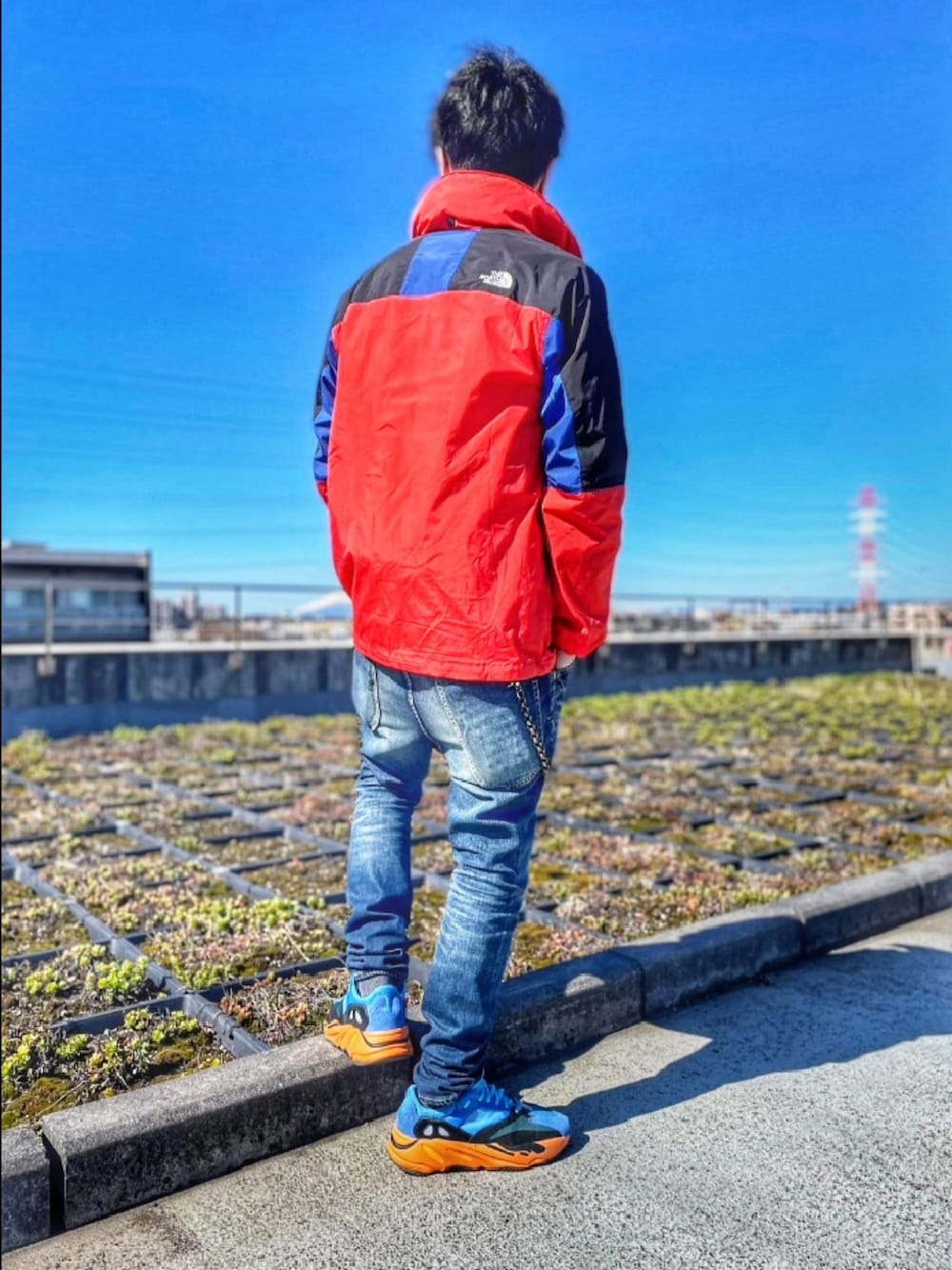 レッド系のナイロンジャケット、ブルー系のデニムパンツ、ブルー系のスニーカーを着用したメンズの春コーディネートの3枚目の写真