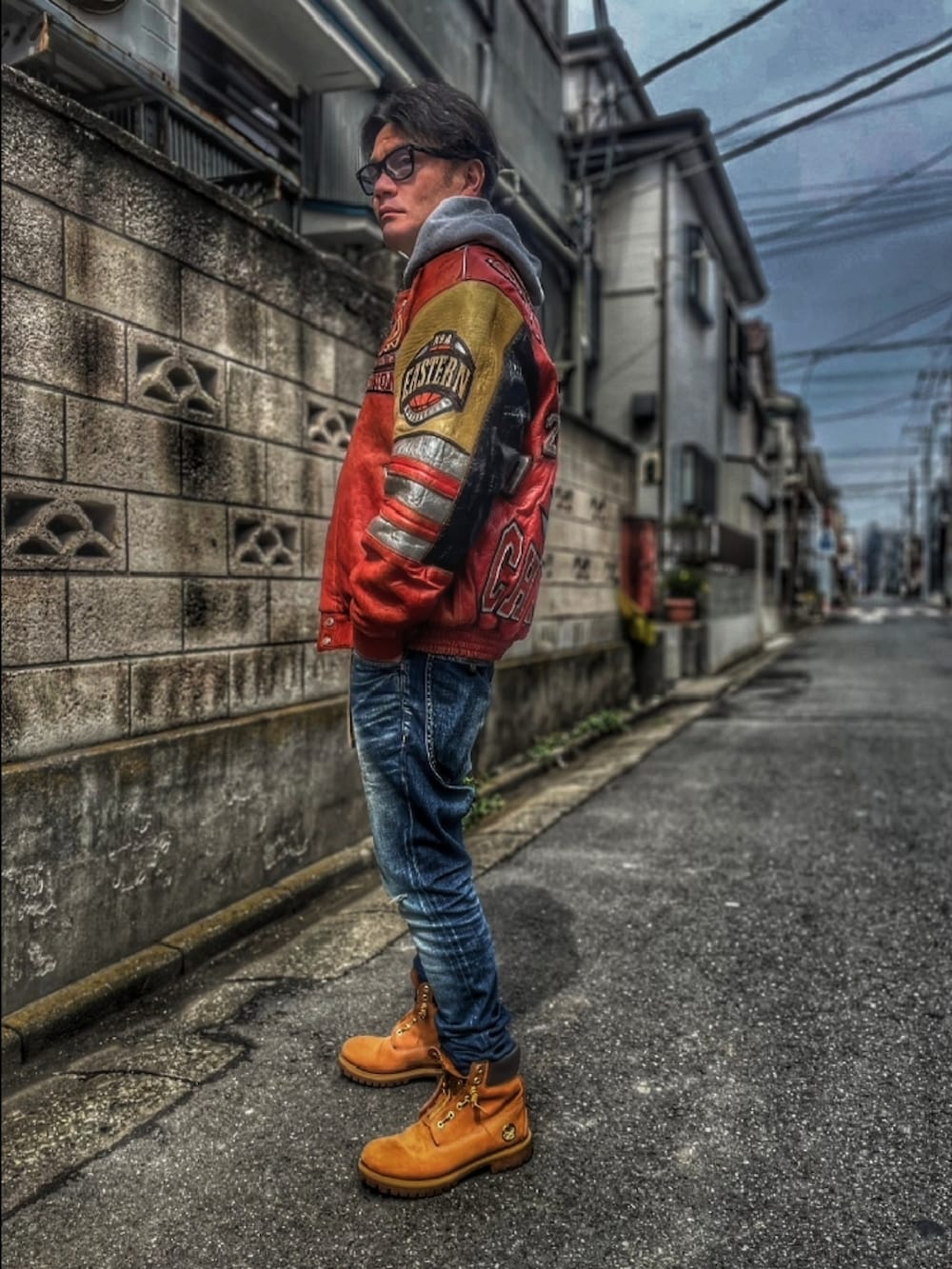 レッド系のスタジャン、ブルー系のデニムパンツ、イエロー系のブーツを着用したメンズの春コーディネートの2枚目の写真