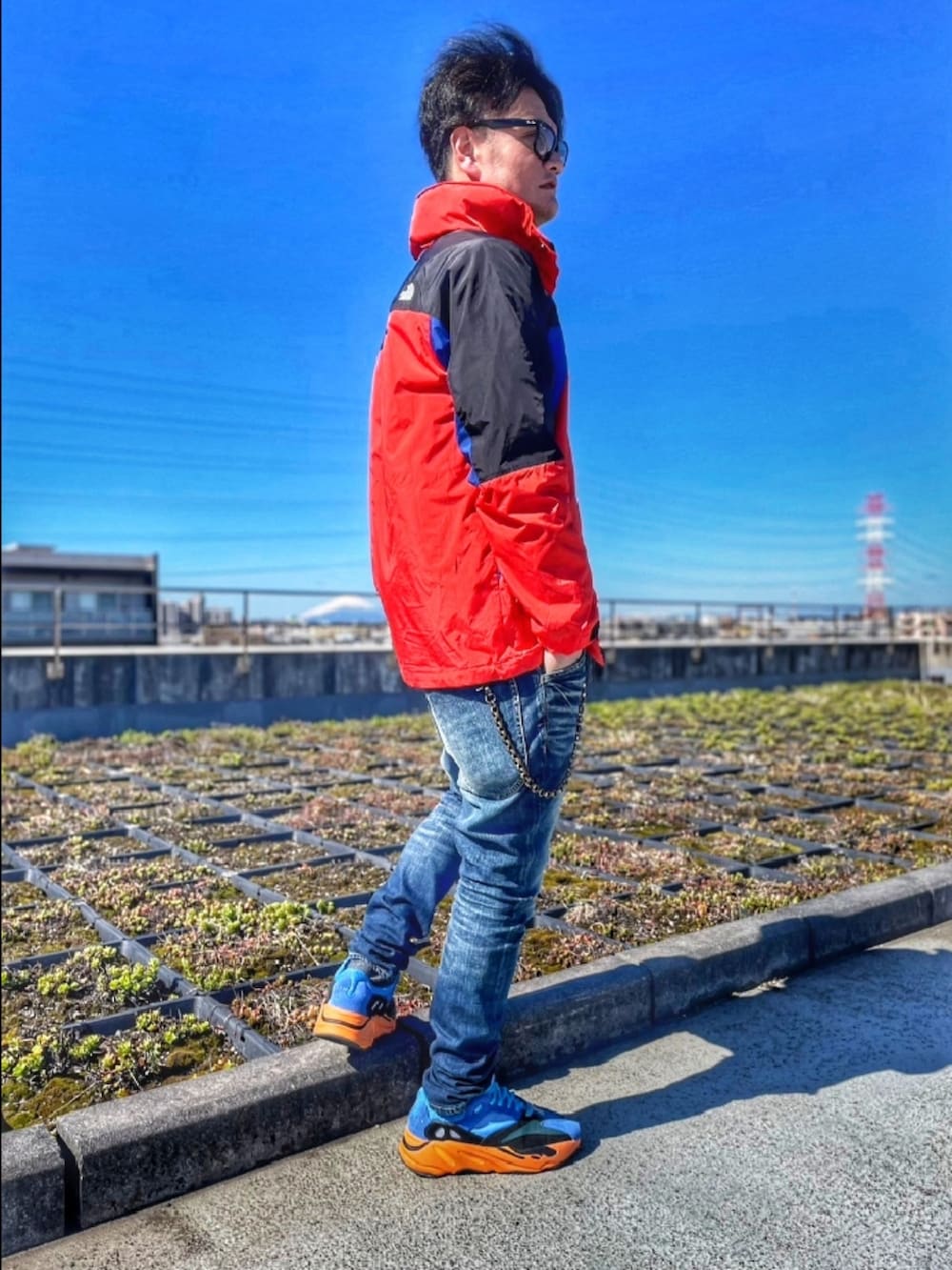 レッド系のナイロンジャケット、ブルー系のデニムパンツ、ブルー系のスニーカーを着用したメンズの春コーディネートの2枚目の写真