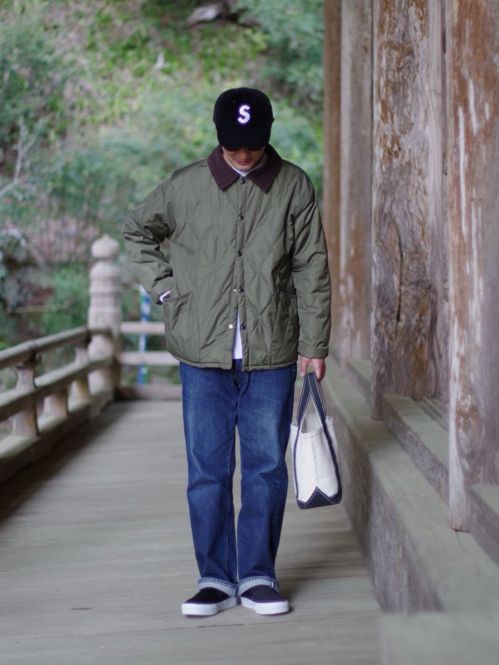 グリーン系のダウンジャケット/コート、ベージュ系のハンドバッグ、ブラック系のスリッポンを着用したメンズの春コーディネートの2枚目の写真