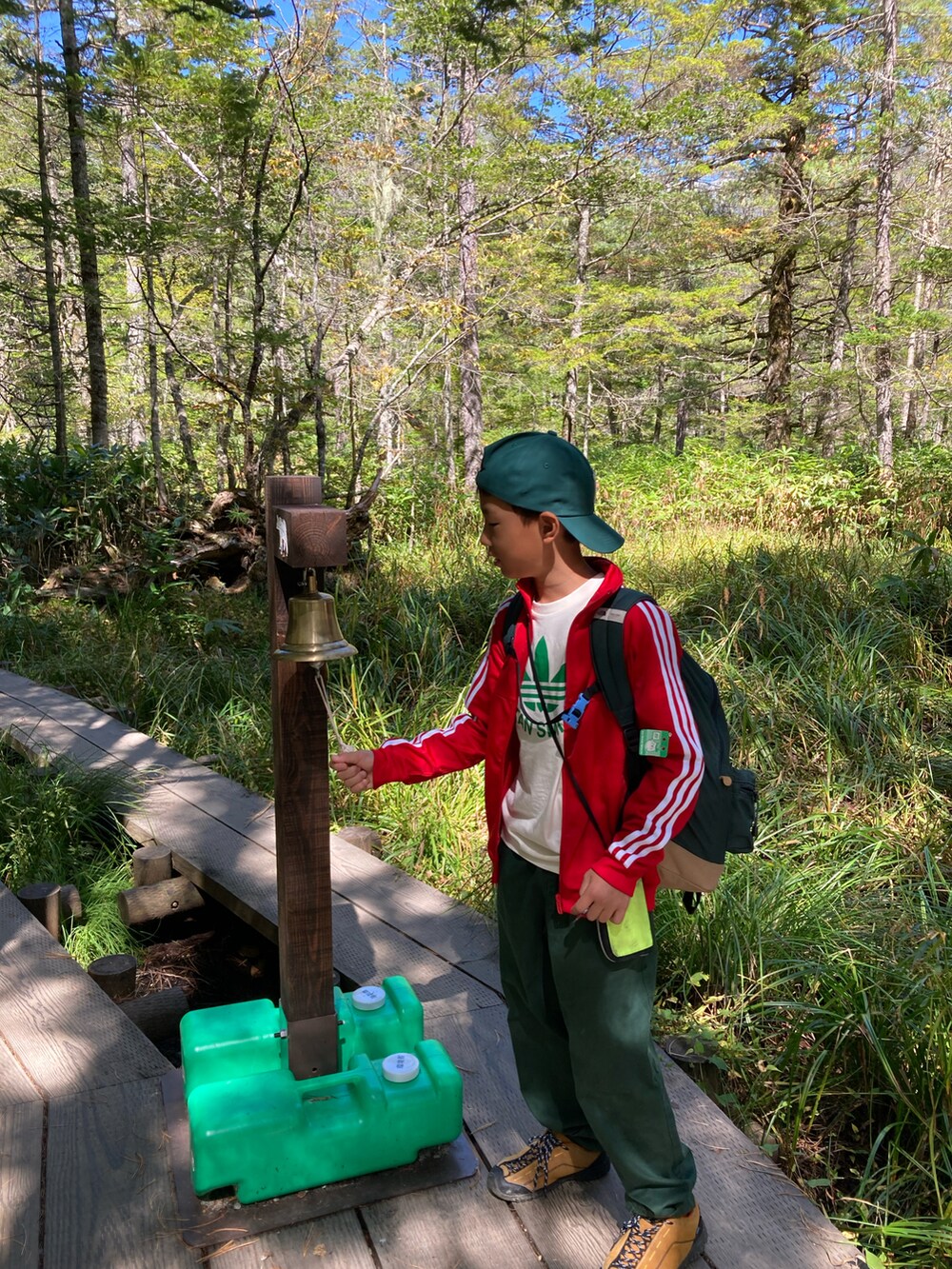 レッド系のジャージ、グリーン系のバックパック/リュック、グリーン系のパンツを着用したキッズの秋コーディネートの2枚目の写真