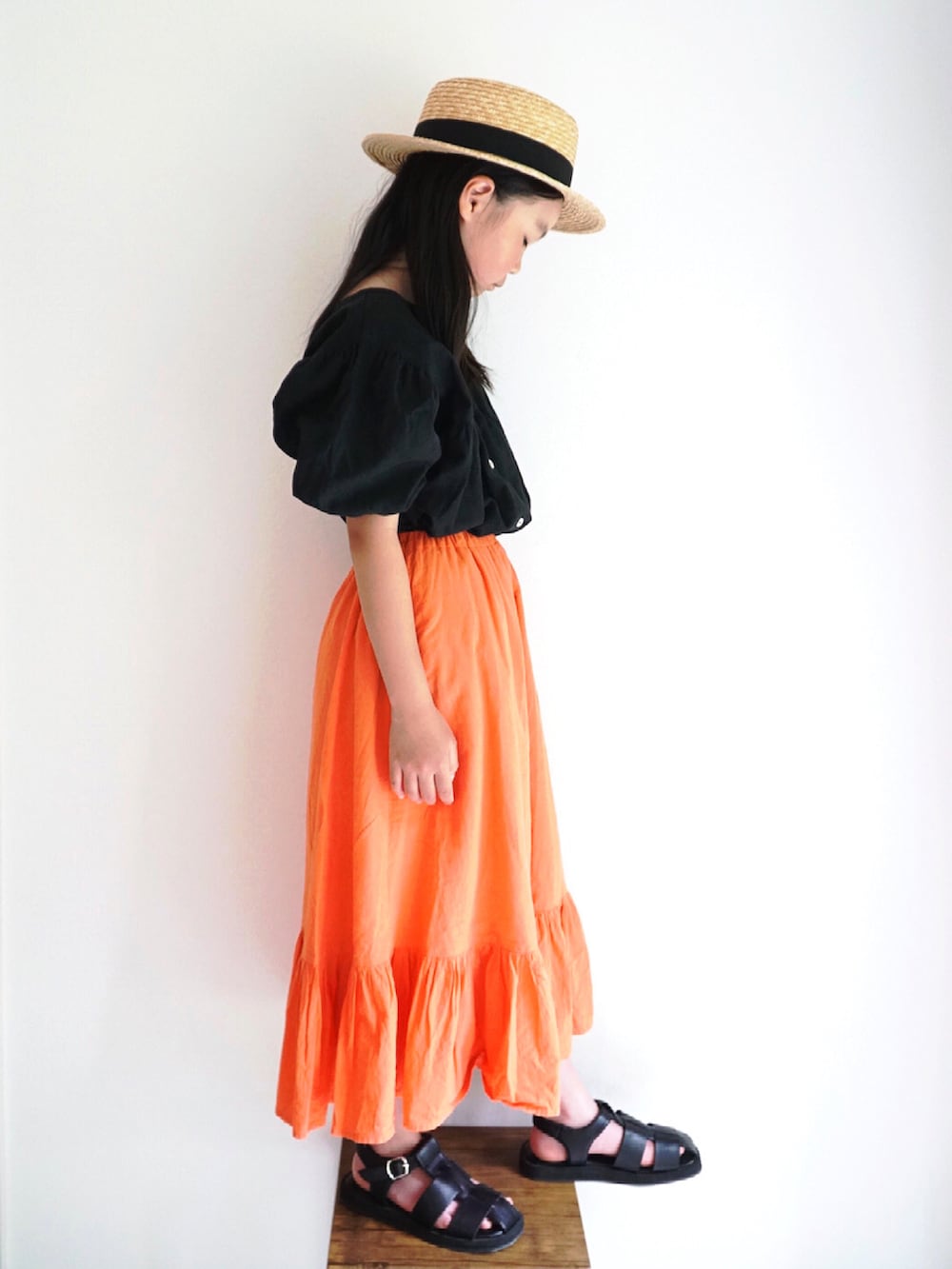 オレンジ系のスカート、ブラック系のサンダル、ブラック系のシャツ/ブラウスを着用したキッズの春コーディネートの2枚目の写真