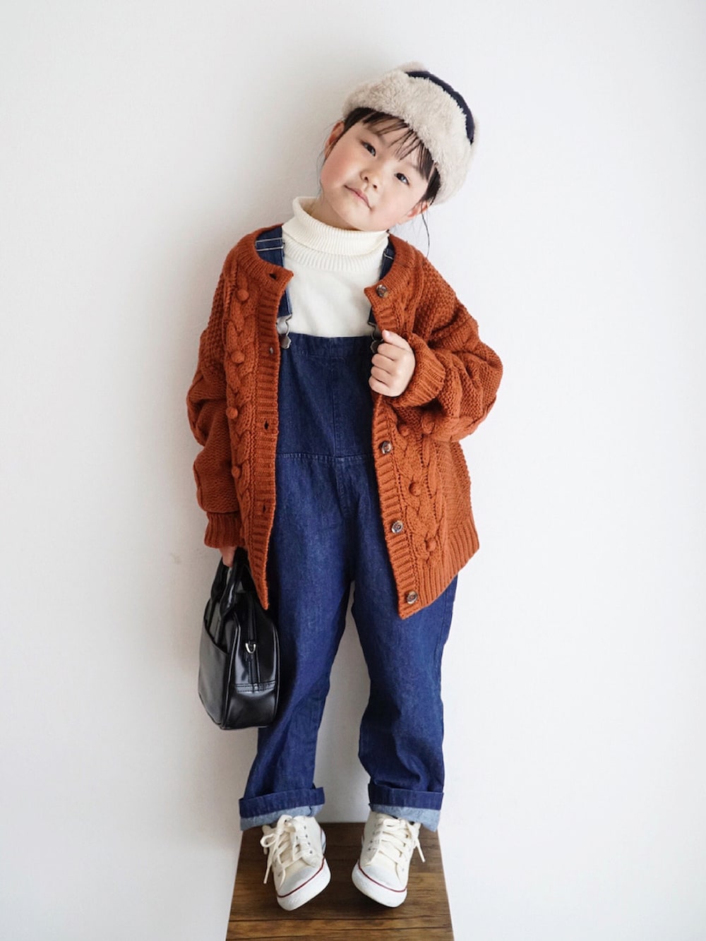 ホワイト系のニット/セーター、ブルー系のサロペット/オーバーオール、オレンジ系のカーディガン/ボレロを着用したキッズの秋コーディネートの2枚目の写真