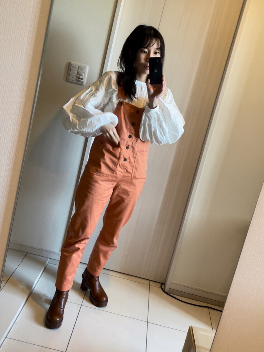 オレンジ系のサロペット/オーバーオール、ホワイト系のシャツ/ブラウス、ブラウン系のブーツを着用したレディースの春コーディネートの3枚目の写真
