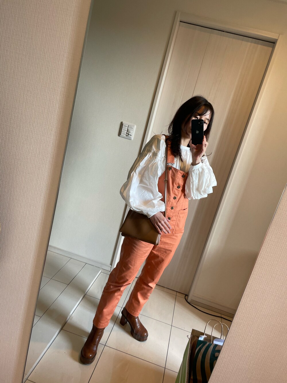 オレンジ系のサロペット/オーバーオール、ホワイト系のシャツ/ブラウス、ブラウン系のブーツを着用したレディースの春コーディネートの5枚目の写真