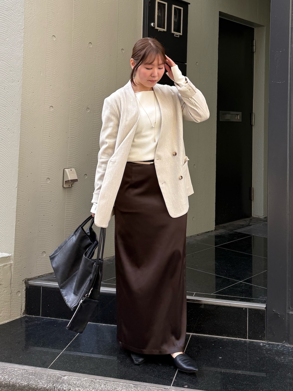 ブラウン系のスカート、ホワイト系のニット/セーター、ブラック系のトートバッグを着用したレディースの冬コーディネートの2枚目の写真
