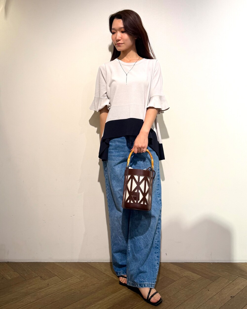 ベージュ系のニット/セーター、ブルー系のデニムパンツ、ブラウン系のハンドバッグを着用したレディースの春コーディネートの2枚目の写真