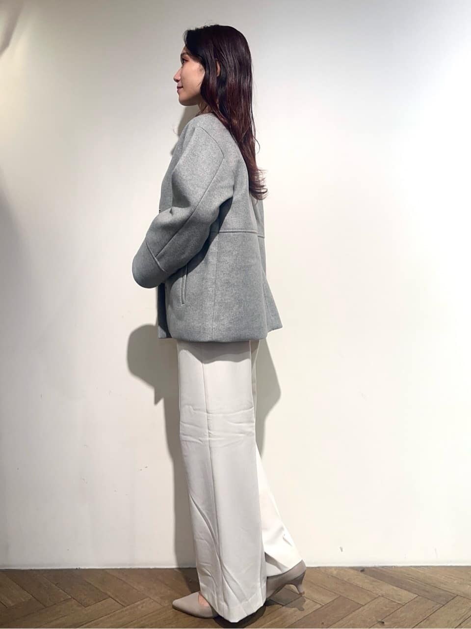 グレー系のノーカラーコート、ブラック系のニット/セーター、ホワイト系のその他パンツを着用したレディースの秋コーディネートの2枚目の写真