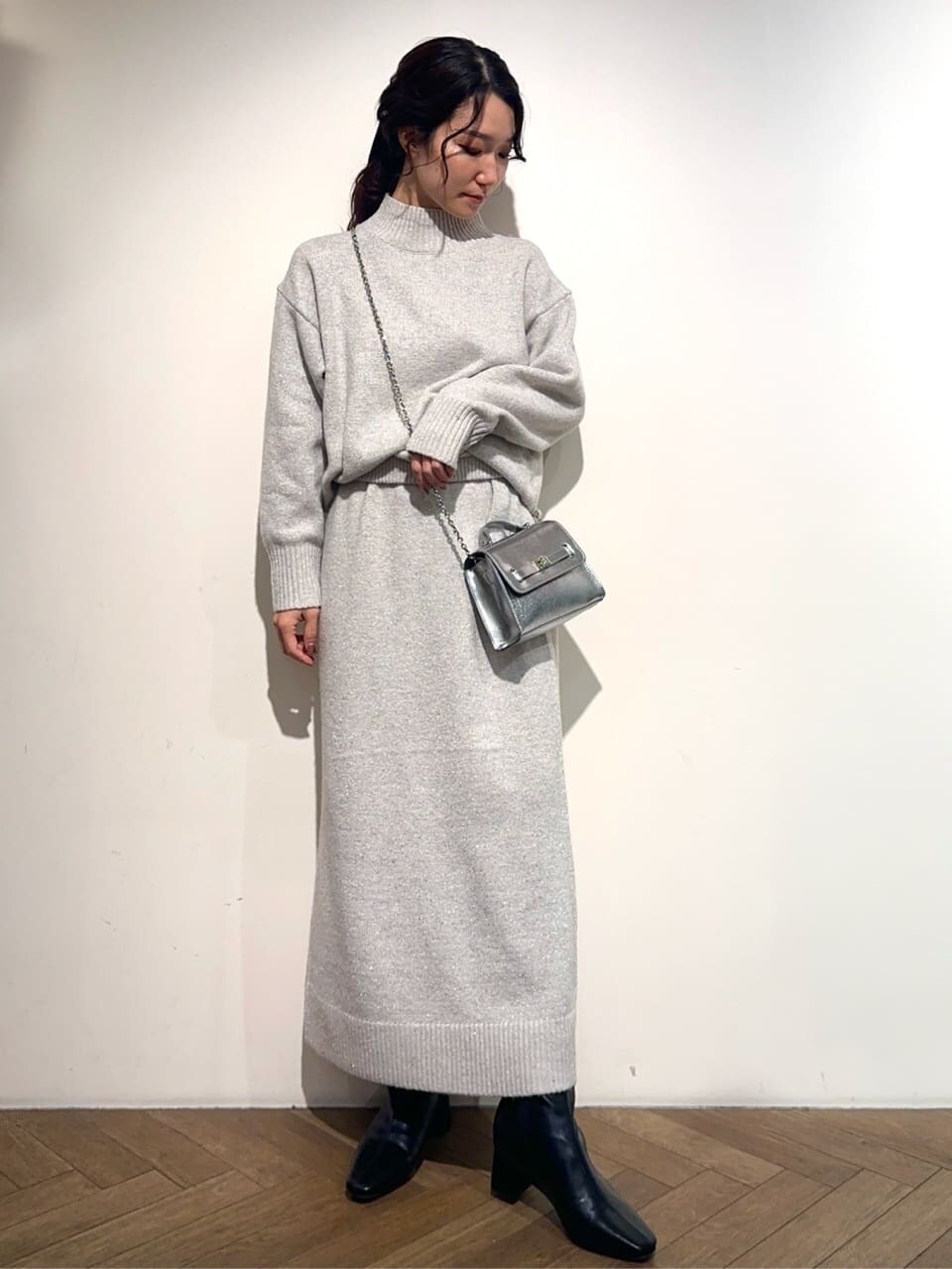 グレー系のニット/セーター、グレー系のスカート、シルバー系のショルダーバッグを着用したレディースの冬コーディネートの2枚目の写真