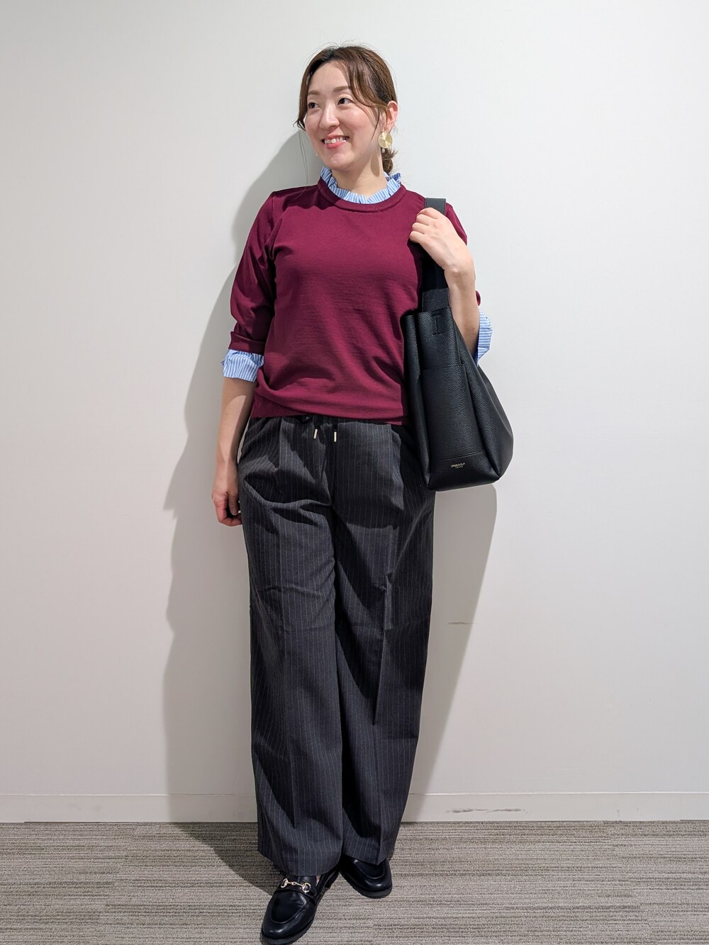 レッド系のニット/セーター、グレー系のその他パンツ、ブラック系のトートバッグを着用したレディースの秋コーディネートの2枚目の写真