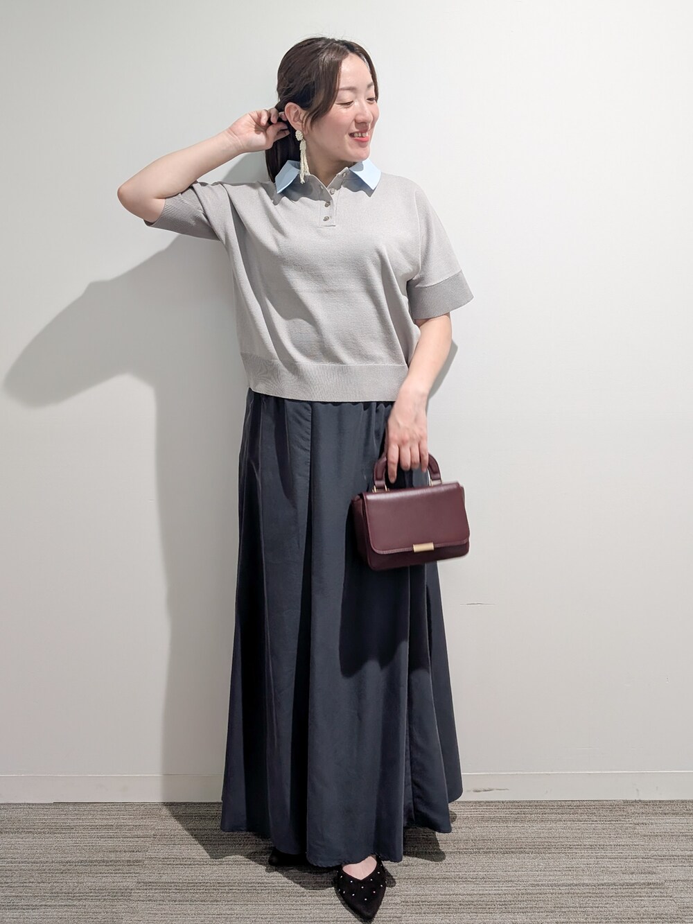 グレー系のニット/セーター、グレー系のスカート、レッド系のショルダーバッグを着用したレディースの夏コーディネートの2枚目の写真