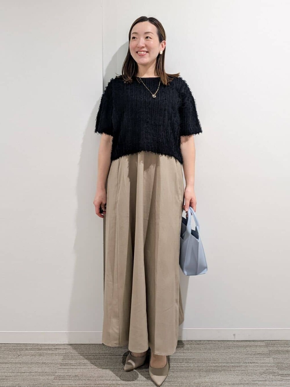 ブラック系のニット/セーター、ベージュ系のワンピース、ブルー系のトートバッグを着用したレディースの夏コーディネートの2枚目の写真