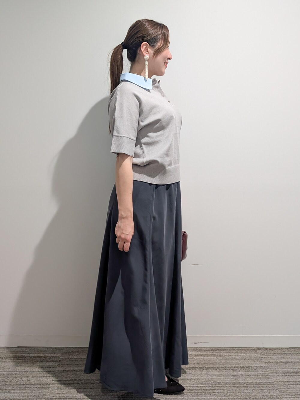グレー系のニット/セーター、グレー系のスカート、レッド系のショルダーバッグを着用したレディースの夏コーディネートの6枚目の写真