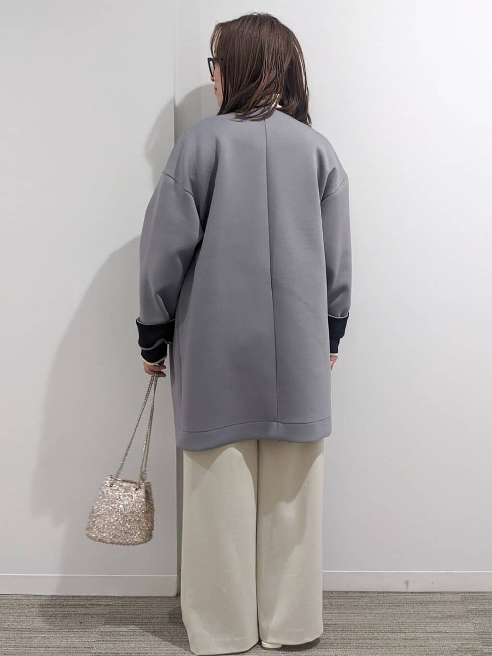 グレー系のノーカラーコート、ブルー系のニット/セーター、ホワイト系のTシャツ/カットソーを着用したレディースの春コーディネートの7枚目の写真