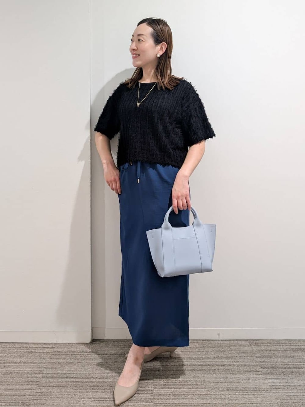 ブラック系のニット/セーター、ブルー系のスカート、ブルー系のトートバッグを着用したレディースの夏コーディネートの4枚目の写真