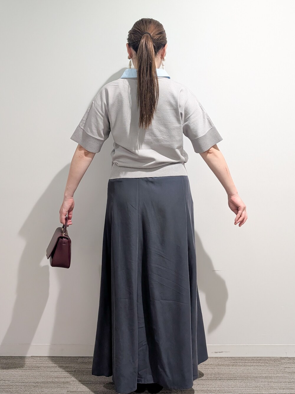 グレー系のニット/セーター、グレー系のスカート、レッド系のショルダーバッグを着用したレディースの夏コーディネートの5枚目の写真