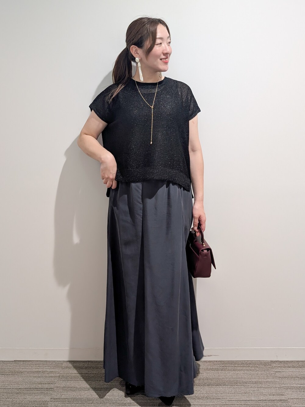 ブラック系のニット/セーター、グレー系のスカート、レッド系のショルダーバッグを着用したレディースの夏コーディネートの3枚目の写真