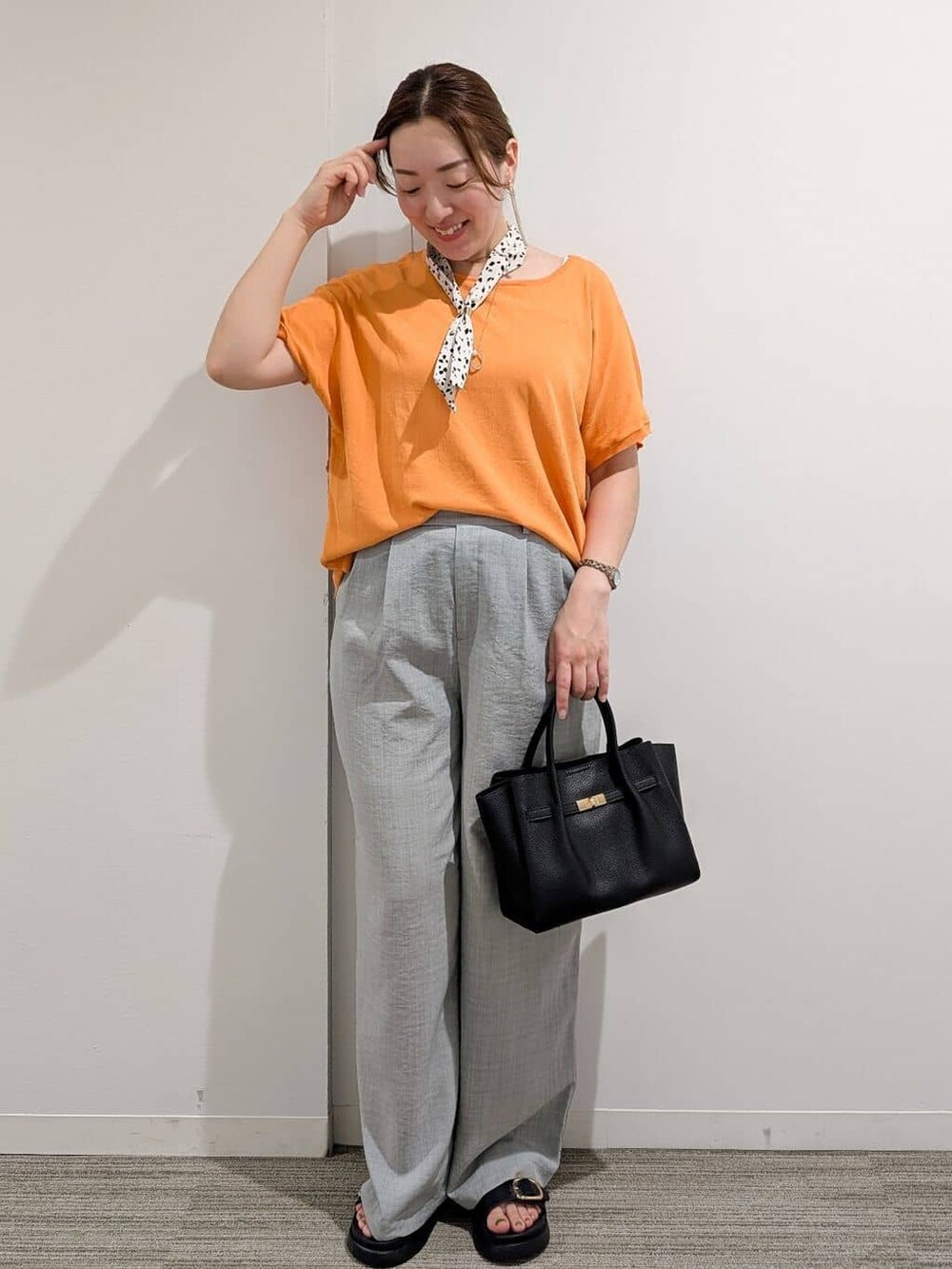 オレンジ系のニット/セーター、グレー系のその他パンツ、ブラック系のサンダルを着用したレディースの夏コーディネートの2枚目の写真