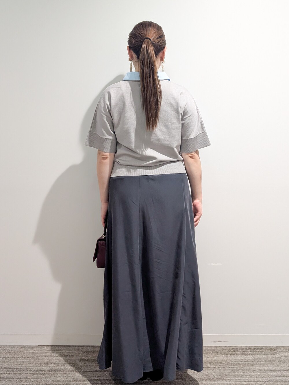 グレー系のニット/セーター、グレー系のスカート、レッド系のショルダーバッグを着用したレディースの夏コーディネートの4枚目の写真