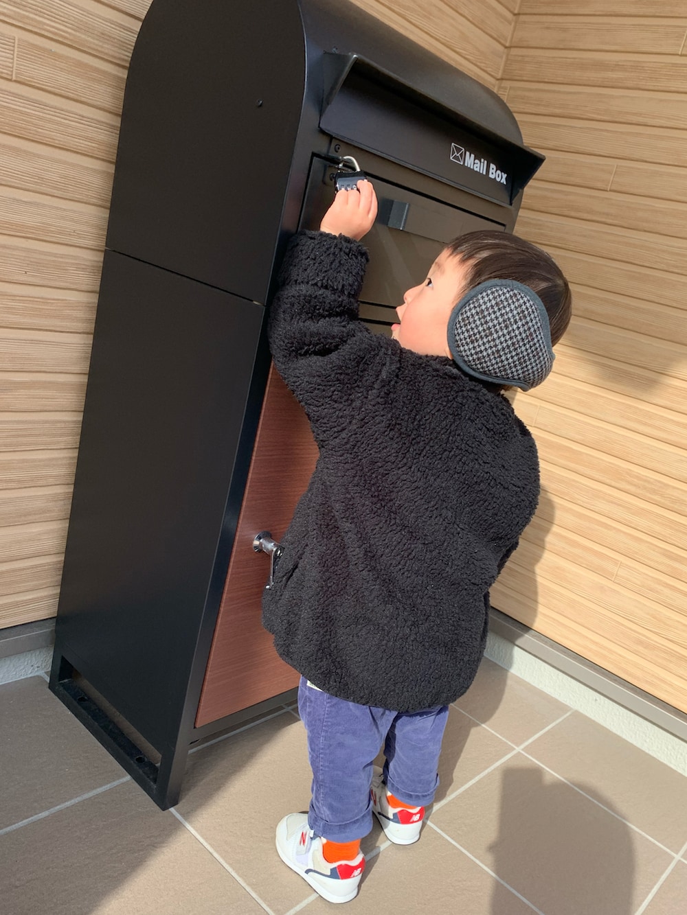 ブラック系のトップス、ホワイト系のスニーカー、グレー系のイヤーマフを着用したメンズの冬コーディネートの4枚目の写真