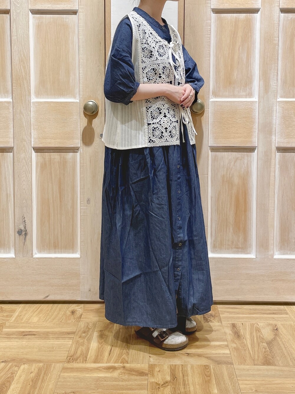 ホワイト系のベスト、ブラック系のかごバッグ、ブラウン系のサンダルを着用したレディースの夏コーディネートの2枚目の写真