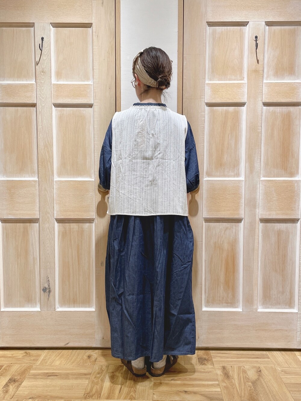 ホワイト系のベスト、ブラック系のかごバッグ、ブラウン系のサンダルを着用したレディースの夏コーディネートの3枚目の写真