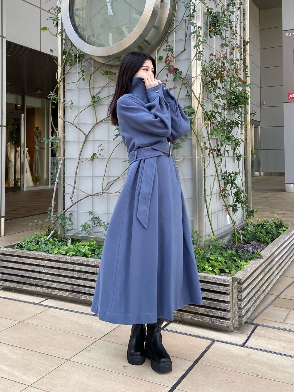 ブルー系のステンカラーコート、ベージュ系のニット/セーター、ブラウン系のスカートを着用したレディースの秋コーディネートの3枚目の写真