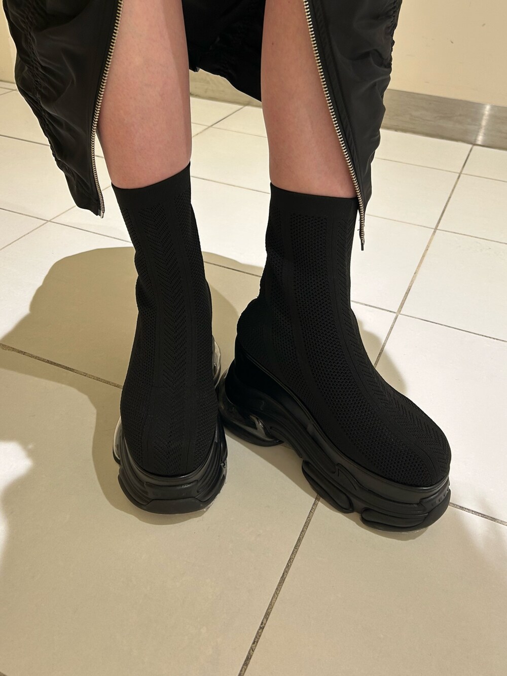 ブラック系のスカート、ブラック系のニット/セーター、ブラック系のブーツを着用したレディースの春コーディネートの6枚目の写真