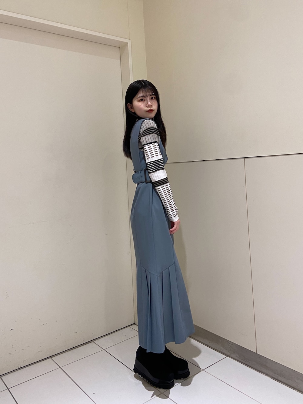 ブルー系のワンピース、ホワイト系のニット/セーター、ブラック系のブーツを着用したレディースの冬コーディネートの2枚目の写真