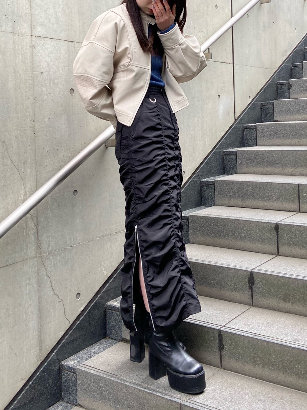 ブラック系のスカート、ブルー系のニット/セーター、ホワイト系のブルゾンを着用したレディースの春コーディネートの2枚目の写真