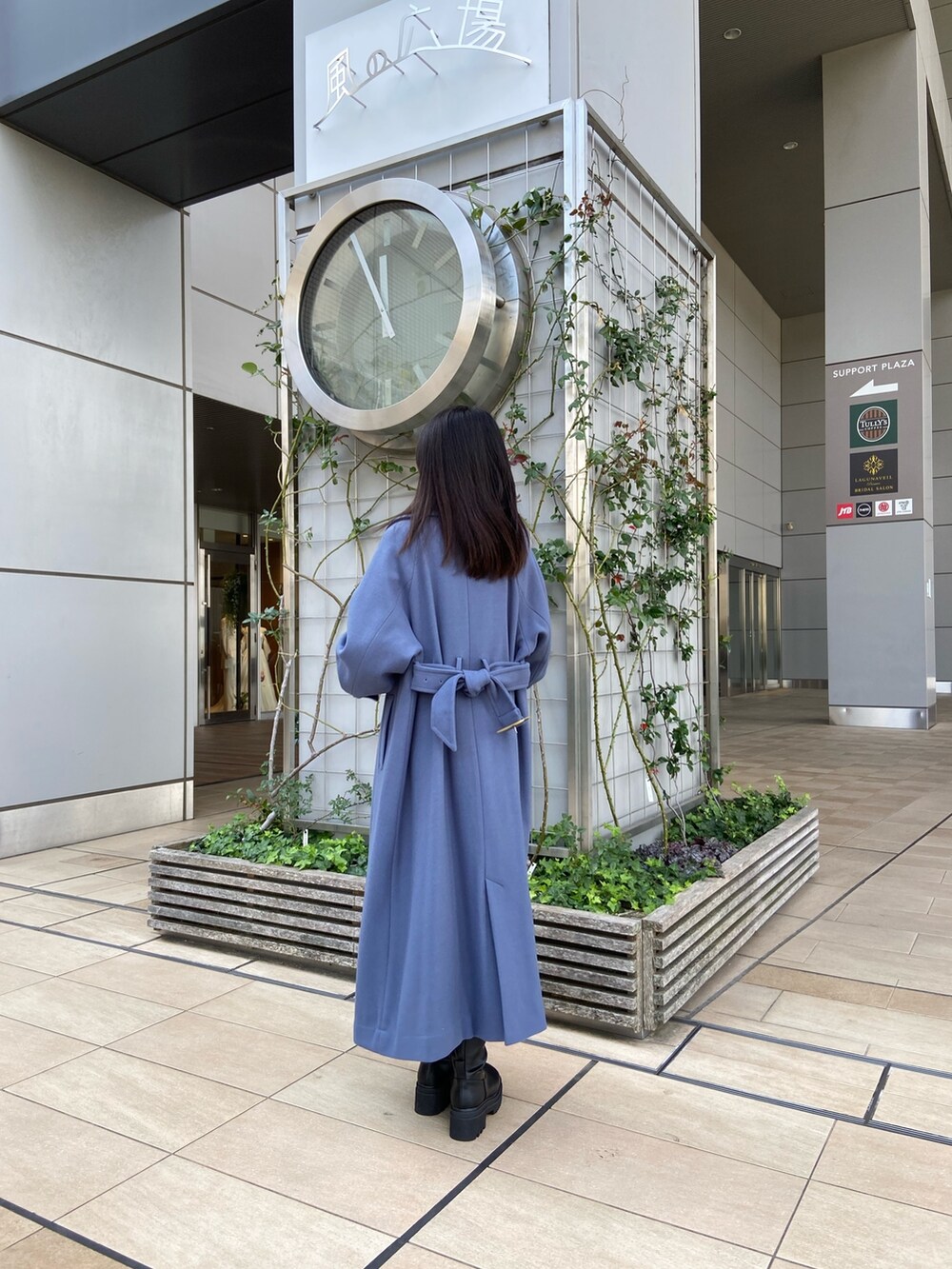 ブルー系のステンカラーコート、ベージュ系のニット/セーター、ブラウン系のスカートを着用したレディースの秋コーディネートの2枚目の写真