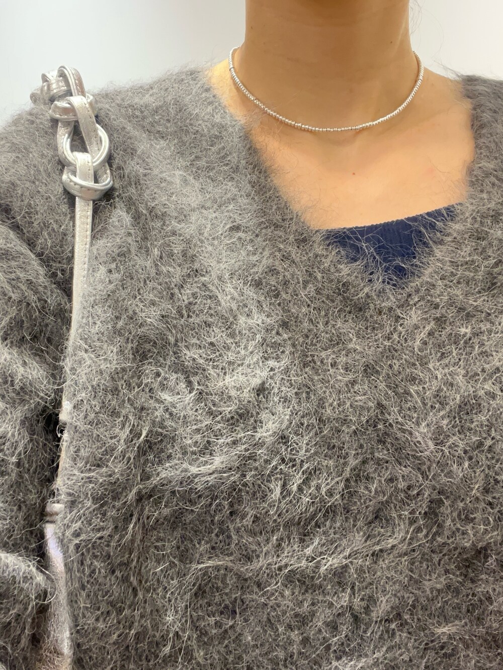 グレー系のニット/セーター、シルバー系のバッグ、ブラック系のデニムパンツを着用したレディースの秋コーディネートの4枚目の写真