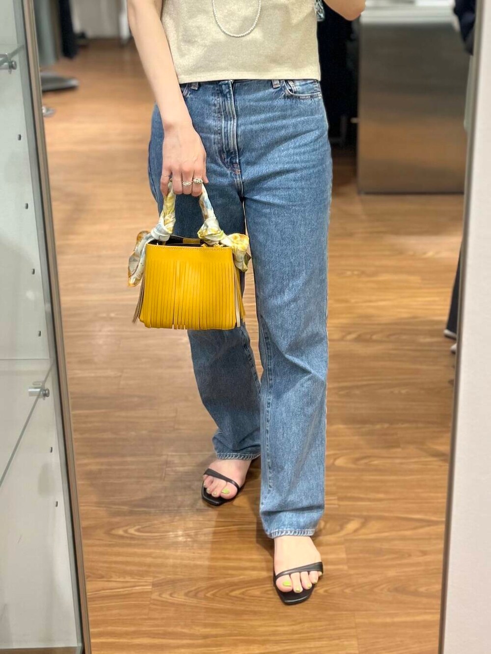 イエロー系のハンドバッグ、ブルー系のデニムパンツ、ゴールド系のTシャツ/カットソーを着用したレディースの春コーディネートの3枚目の写真