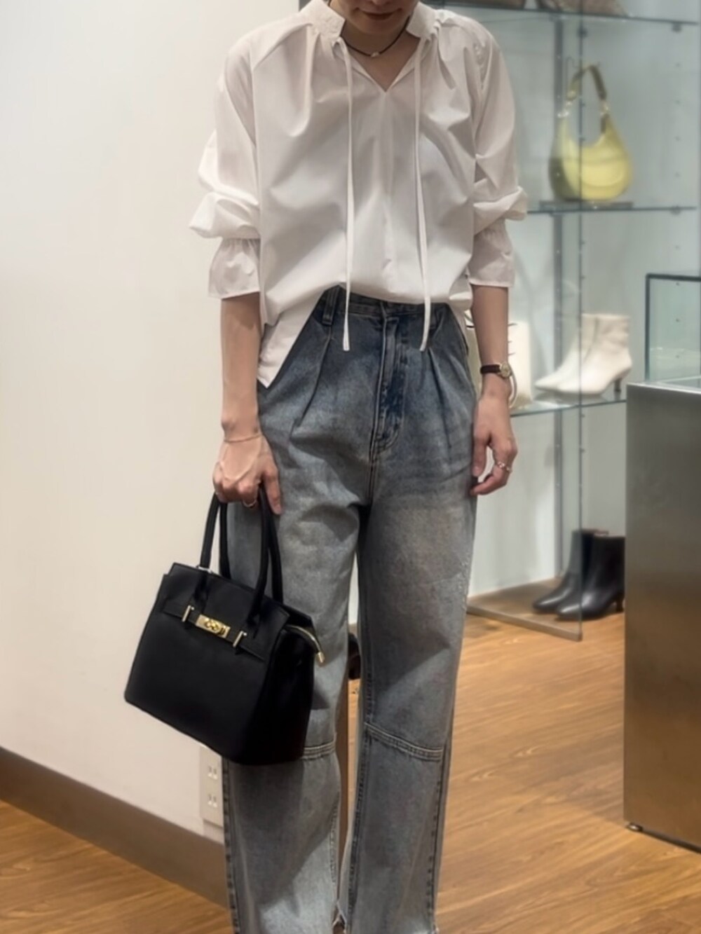 ブラック系のハンドバッグ、ブラック系のパンプス、ブルー系のデニムパンツを着用したレディースの秋コーディネートの3枚目の写真