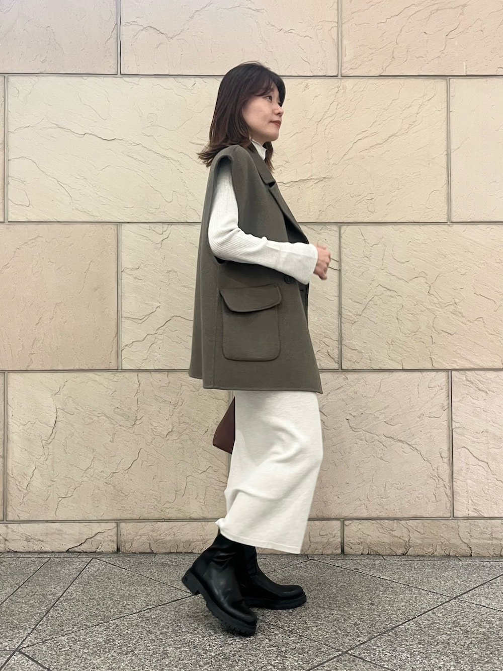 ブラウン系のハンドバッグ、ブラック系のブーツ、グリーン系のその他アウターを着用したレディースの秋コーディネートの4枚目の写真