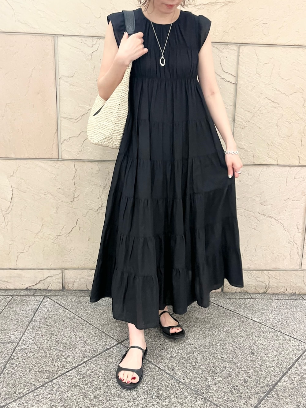 ベージュ系のかごバッグ、ブラック系のワンピース、ブラック系のサンダルを着用したレディースの夏コーディネートの5枚目の写真