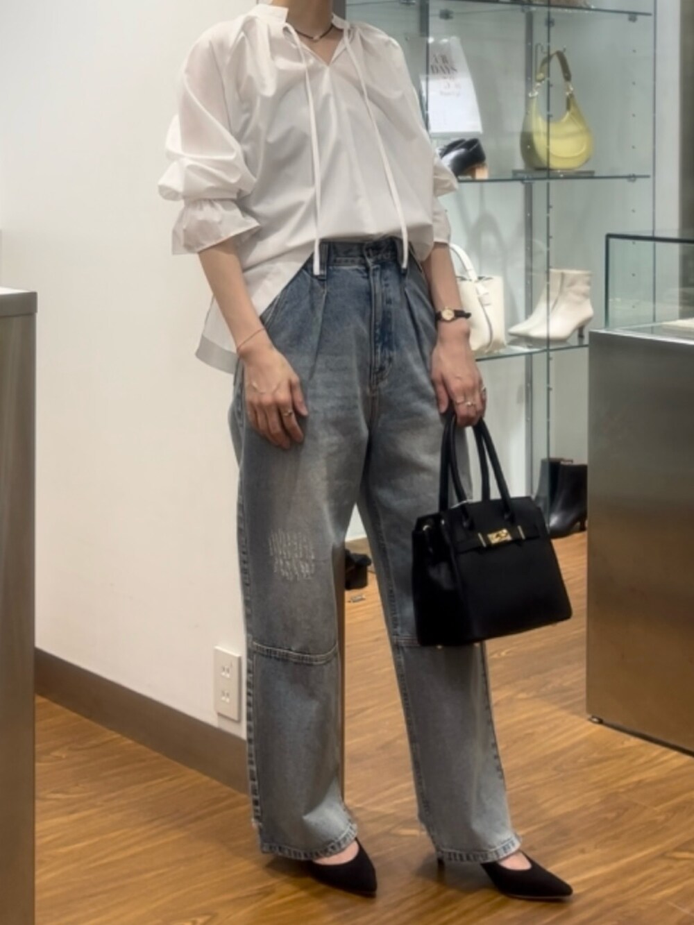 ブラック系のハンドバッグ、ブラック系のパンプス、ブルー系のデニムパンツを着用したレディースの秋コーディネートの4枚目の写真